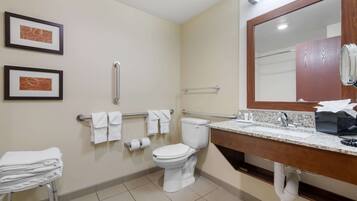 A modern bathroom with a toilet, sink, and handrails. There are framed pictures on the wall and a towel rack with towels.
