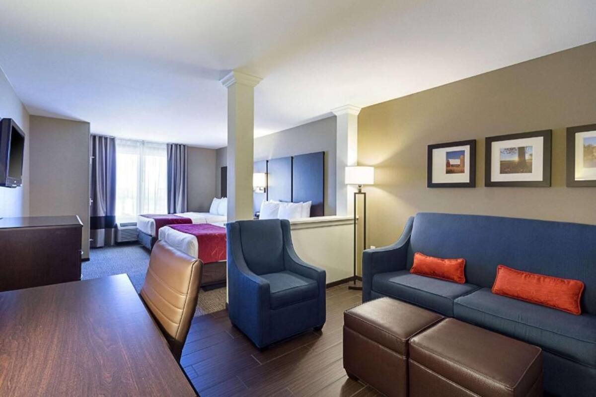 A hotel room with a bed, a desk, a chair, a sofa, and a TV.