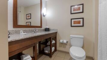 A bathroom with a granite countertop, a wooden vanity, a white toilet, and two framed pictures on the wall.