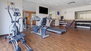 Een sportschool met loopbanden, elliptische trainers en een gewichtbank.