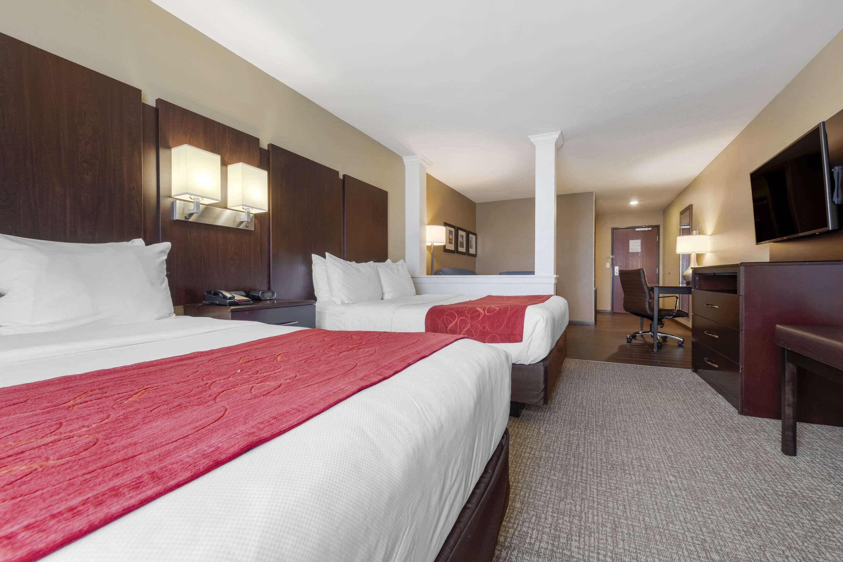 A hotel room with two beds, a desk, a chair, a TV, and a lamp.