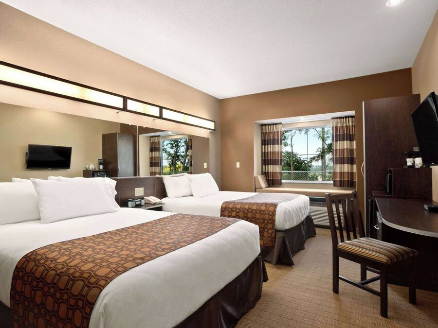 A hotel room with two beds, a desk, a chair, a TV, and a window with curtains.