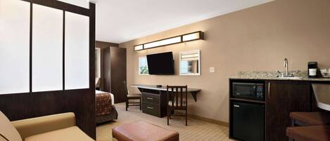 Una habitación de hotel compacta con kitchenette, un sofá, un escritorio y televisión.