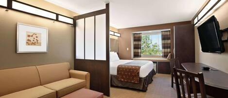 A hotel room with a bed, a sofa, a desk, and a television.