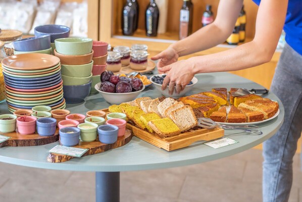 A buffet table with various food items and colorful bowls. - Naturena (Barcelos)