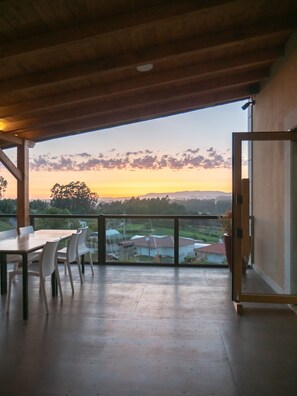 An open balcony with a view of a sunset, a table with chairs, and a wooden ceiling. - Naturena (Barcelos)