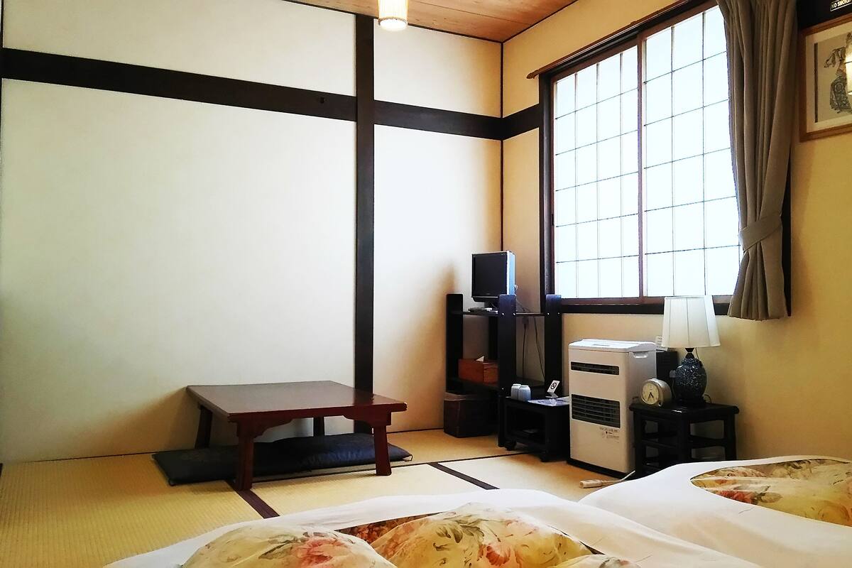 A traditional Japanese room with tatami flooring, a low table, a TV, a heater, and a lamp.