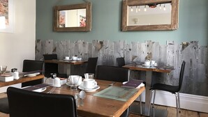 A dining area with wooden tables and black chairs, equipped with white tableware and glassware. - St Bernards Guesthouse (Newquay)