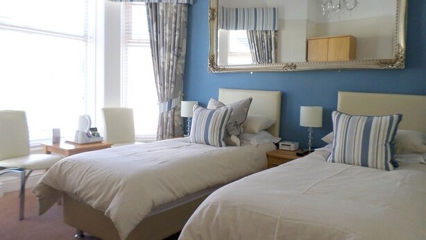 A hotel room with two beds, a large mirror, a chandelier, and a view of the outdoors. - St Bernards Guesthouse (Newquay)