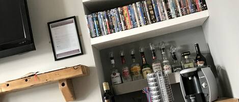A bar area with shelves of DVDs, bottles of alcohol, and a coffee machine.