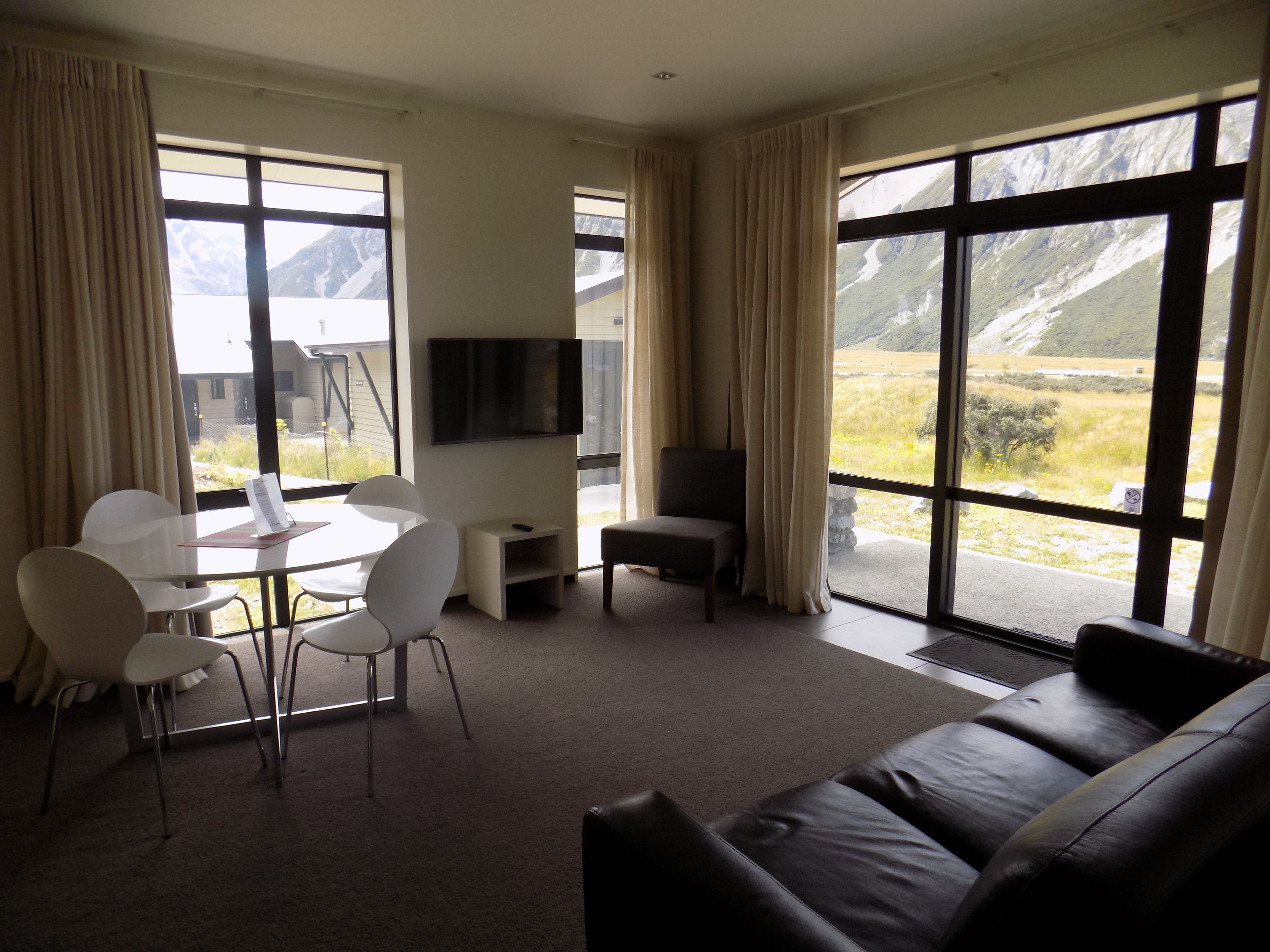 A modern living room with a dining area, a flat-screen TV, and large windows offering mountain views.