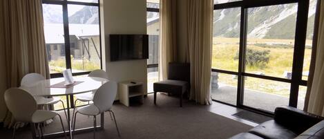 A modern living room with a dining area, a flat-screen TV, and large windows offering mountain views.