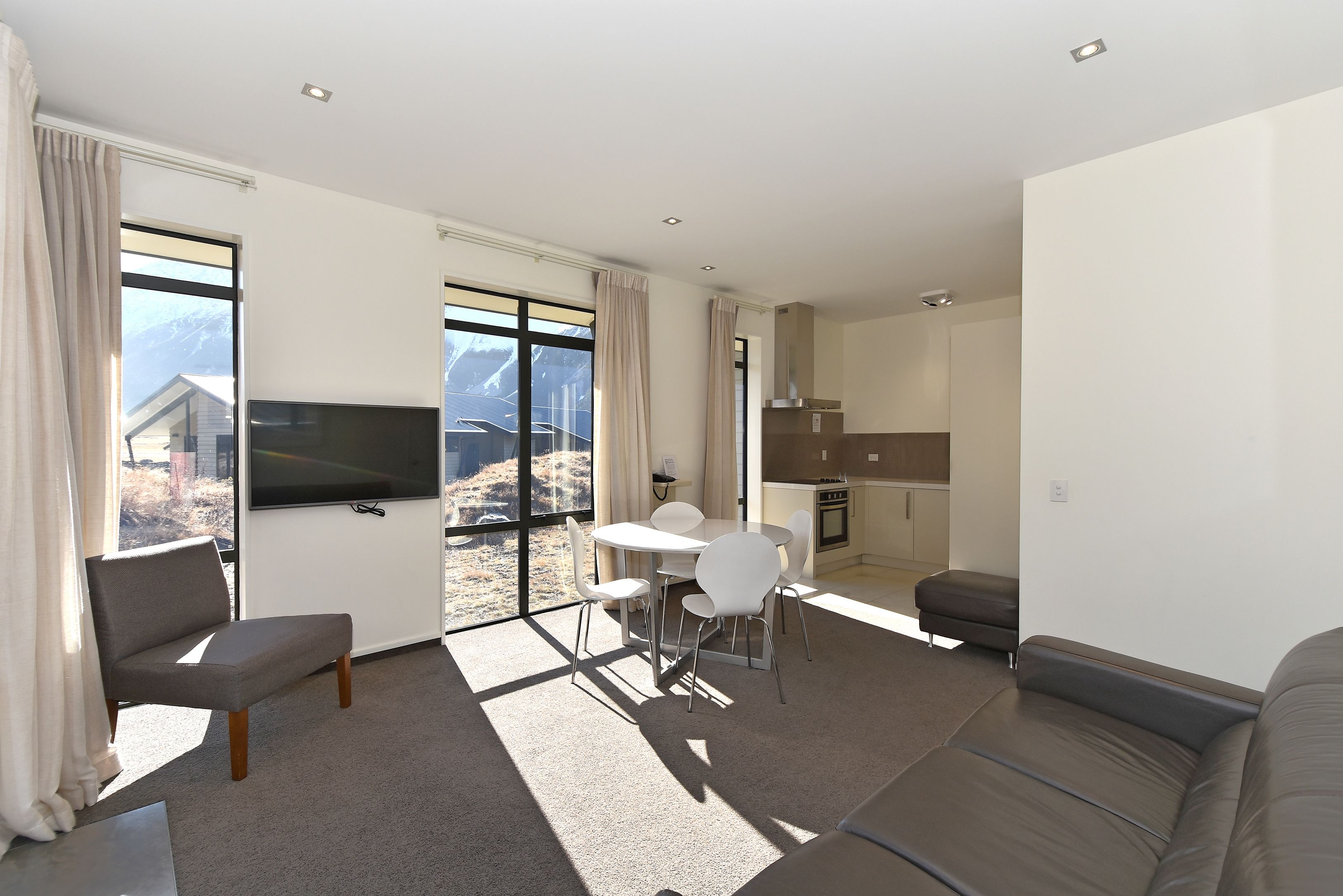 A modern living room with a sofa, a dining table with chairs, a flat-screen TV, and a kitchen area.