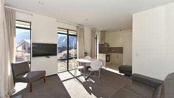 A modern living room with a sofa, a dining table with chairs, a flat-screen TV, and a kitchen area.