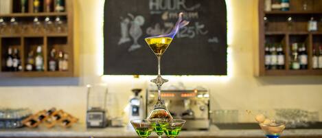 Zona de bar con un letrero de 'Happy Hour', una copa de martini con una guarnición en llamas y dos copas más sobre una bandeja.