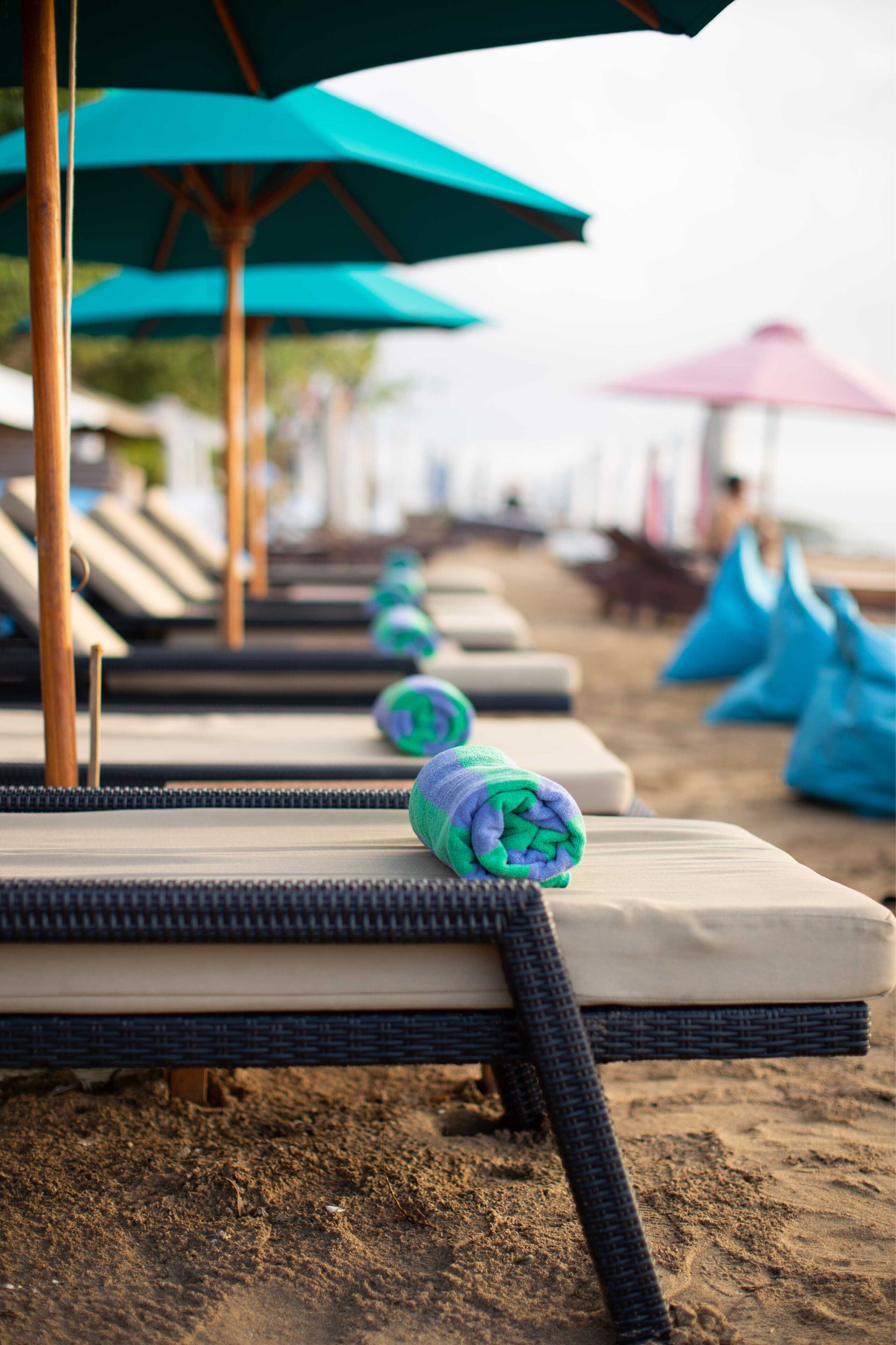 Een rij strandstoelen met parasols, een zandstrand en een verre horizon van de oceaan.