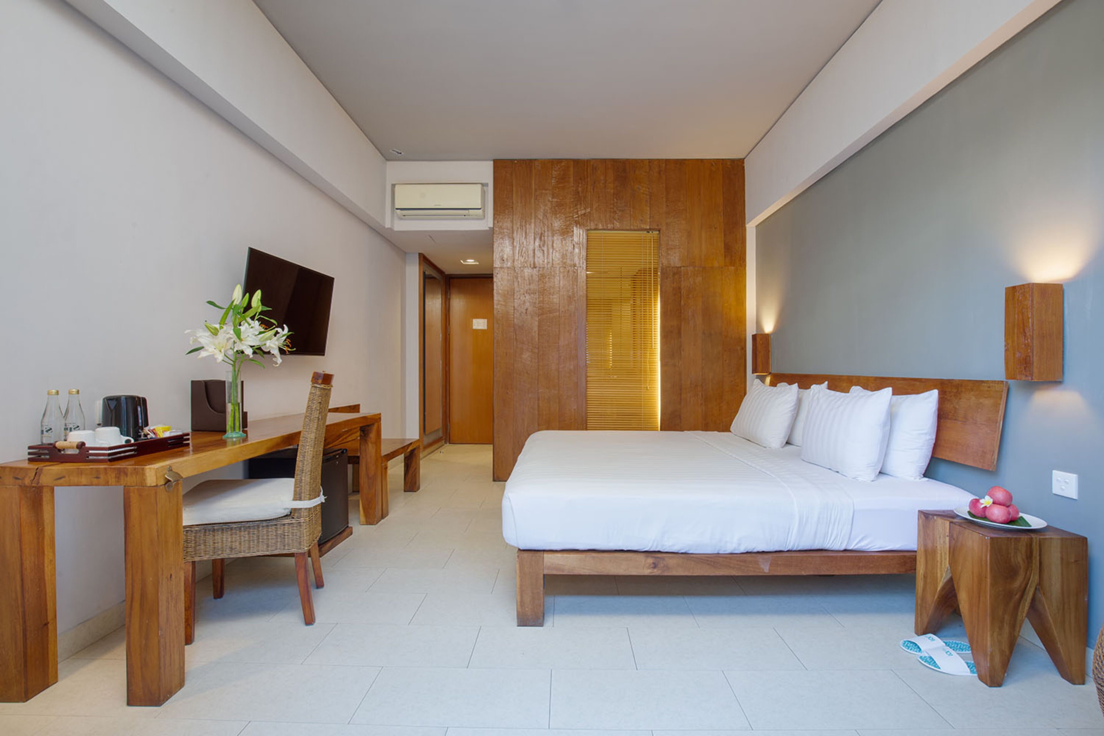 Une chambre d’hôtel moderne avec un lit en bois, un bureau, une chaise et un téléviseur fixé au mur.