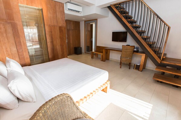 Un dormitorio con una cama grande, un escritorio de madera, una silla, un televisor y una escalera.