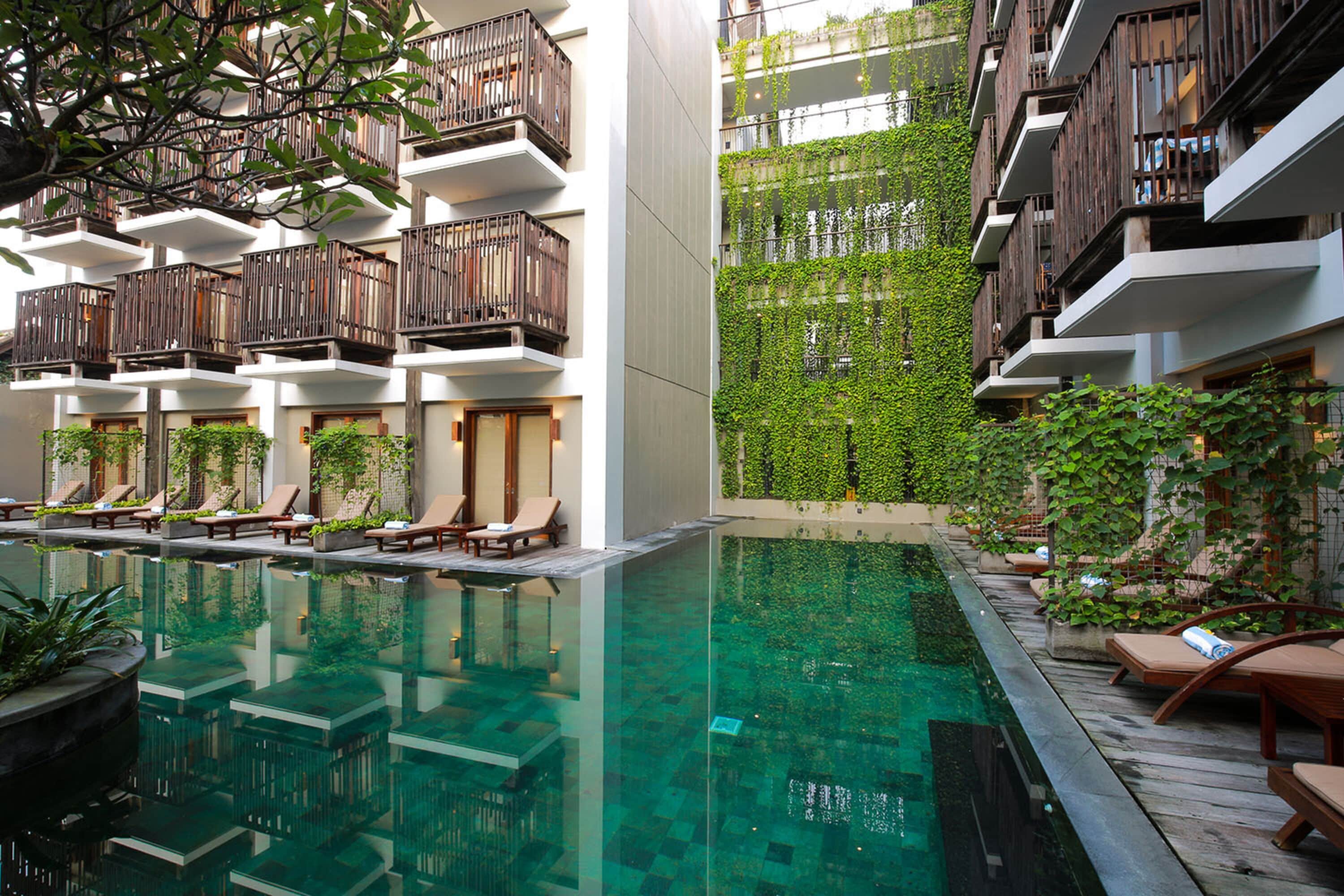 Um hotel moderno com piscina, varandas de madeira e vegetação exuberante.