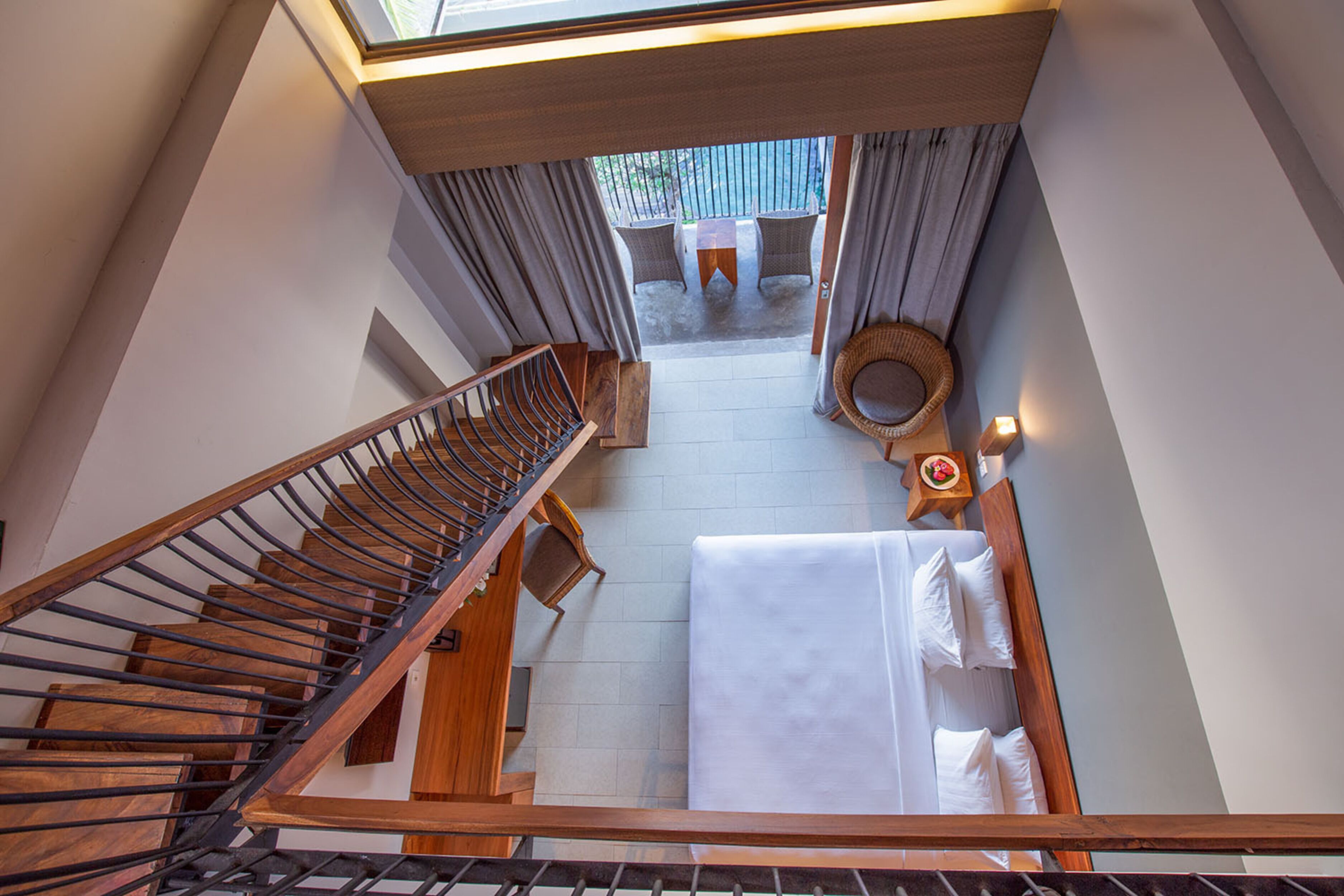 Habitación de hotel con escalera de madera, cama con ropa blanca, una mesita con una vela y vistas al exterior por una ventana.