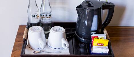 A tray with two white cups, two bottles, a black coffee pot, and some snacks.