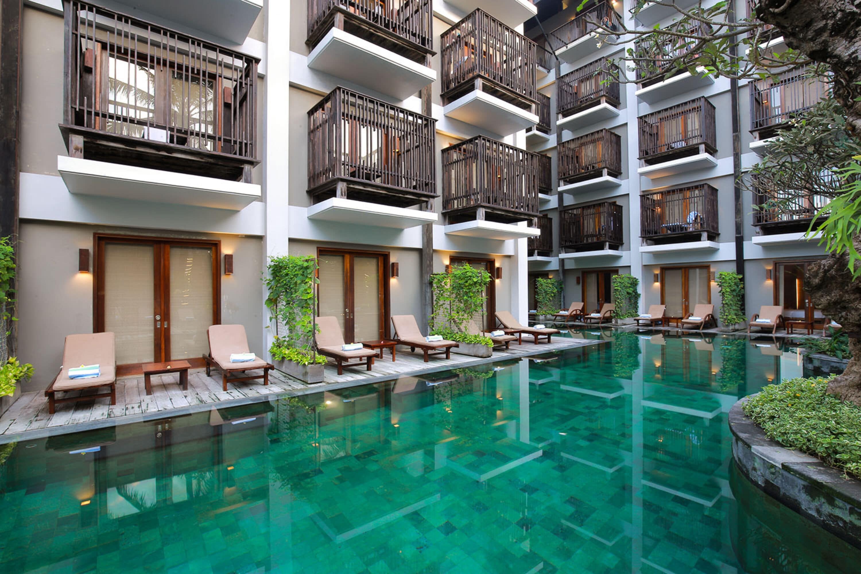 A multi-story hotel with a rooftop pool area, featuring lounge chairs and a clear pool.