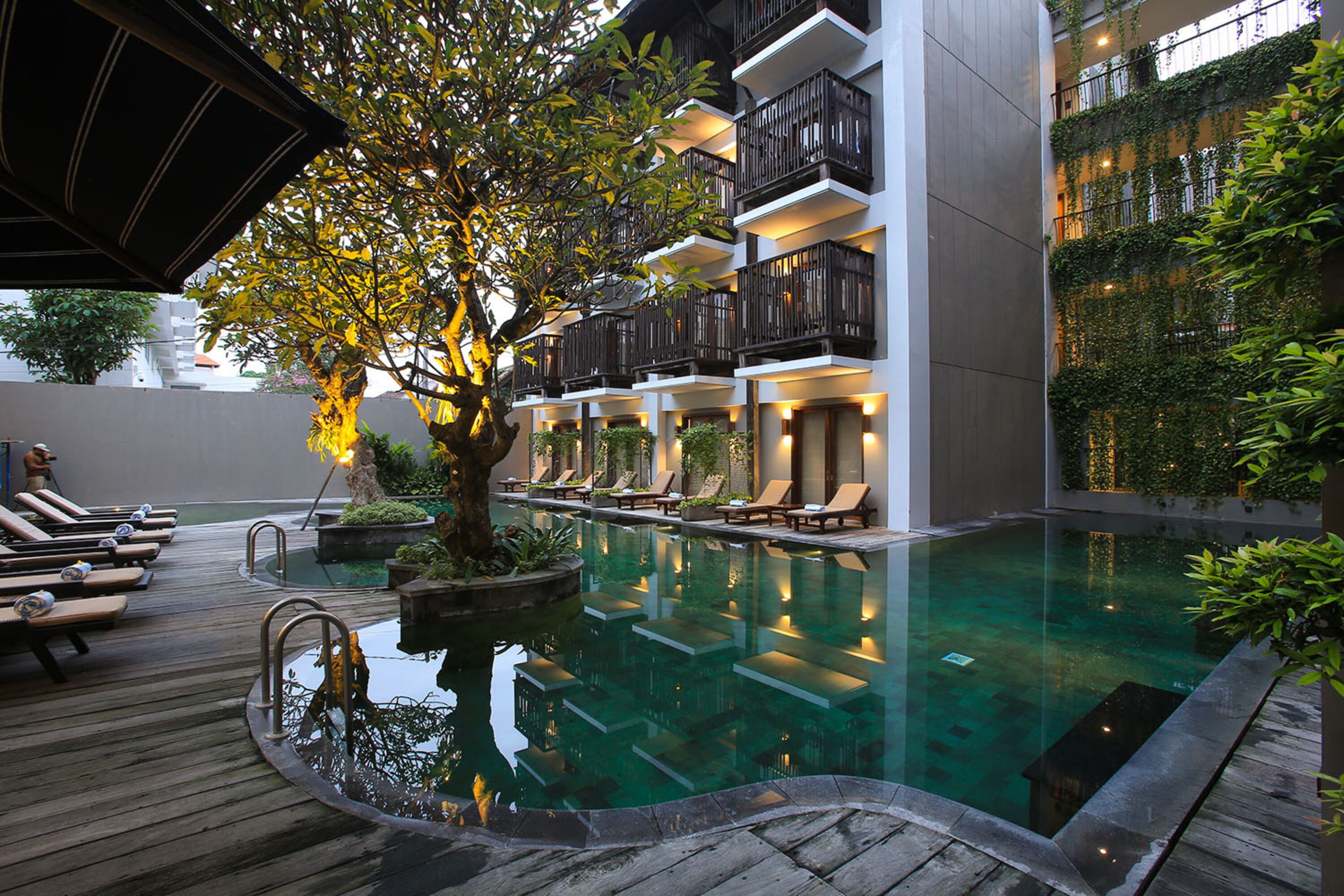 A pool area with lounge chairs and a tree.