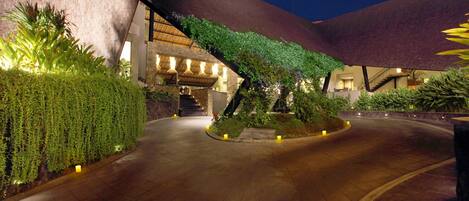 A curved pathway leading to a building with a unique architectural design, surrounded by well-maintained greenery and illuminated by ambient lighting.