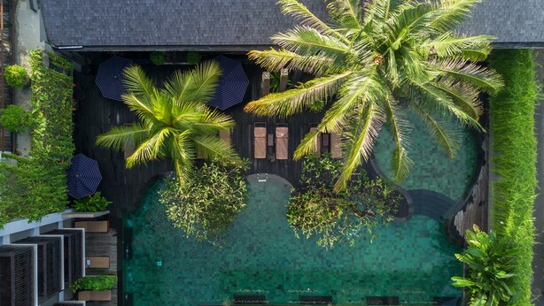 Vista aérea de un resort con piscina cristalina, palmeras y zonas de descanso.