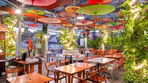 Un comedor interior con varias mesas y sillas, rodeado de sombrillas coloridas y plantas.