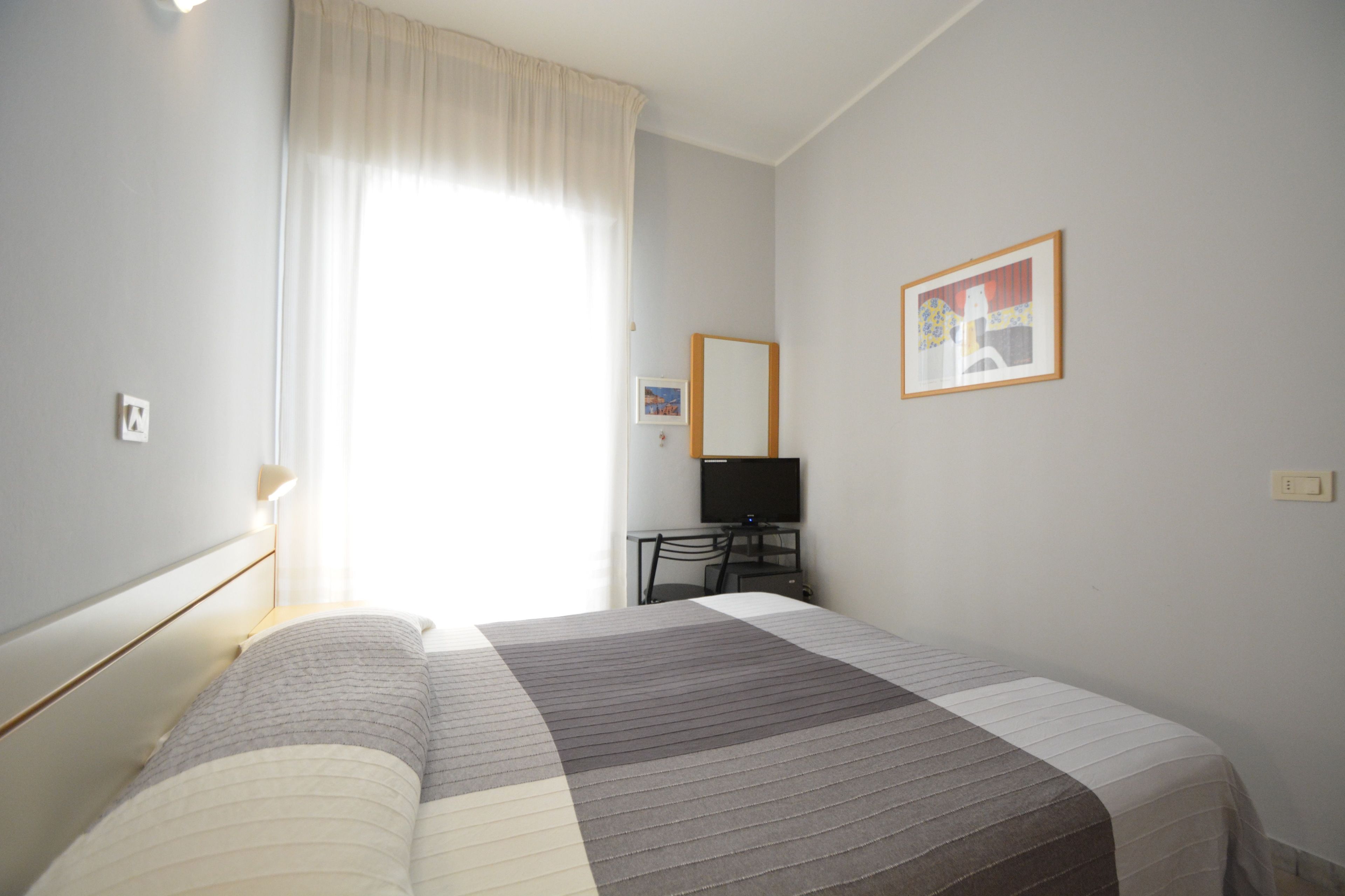 Une chambre d’hôtel équipée d’un lit, d’un bureau, d’une chaise, d’une télévision et d’un tableau encadré au mur.