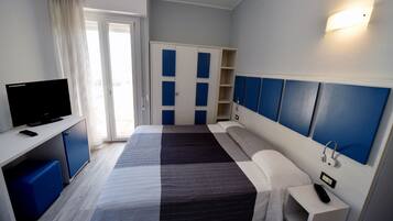 Ein Hotelzimmer mit einem Bett, einem Schreibtisch mit Fernseher, einem Kleiderschrank und einem Nachttisch mit Lampe und Telefon.