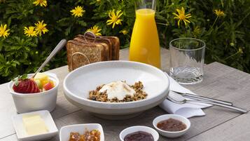 Une table en bois dressée pour le petit-déjeuner, avec des toasts, des céréales, des fruits et du jus.