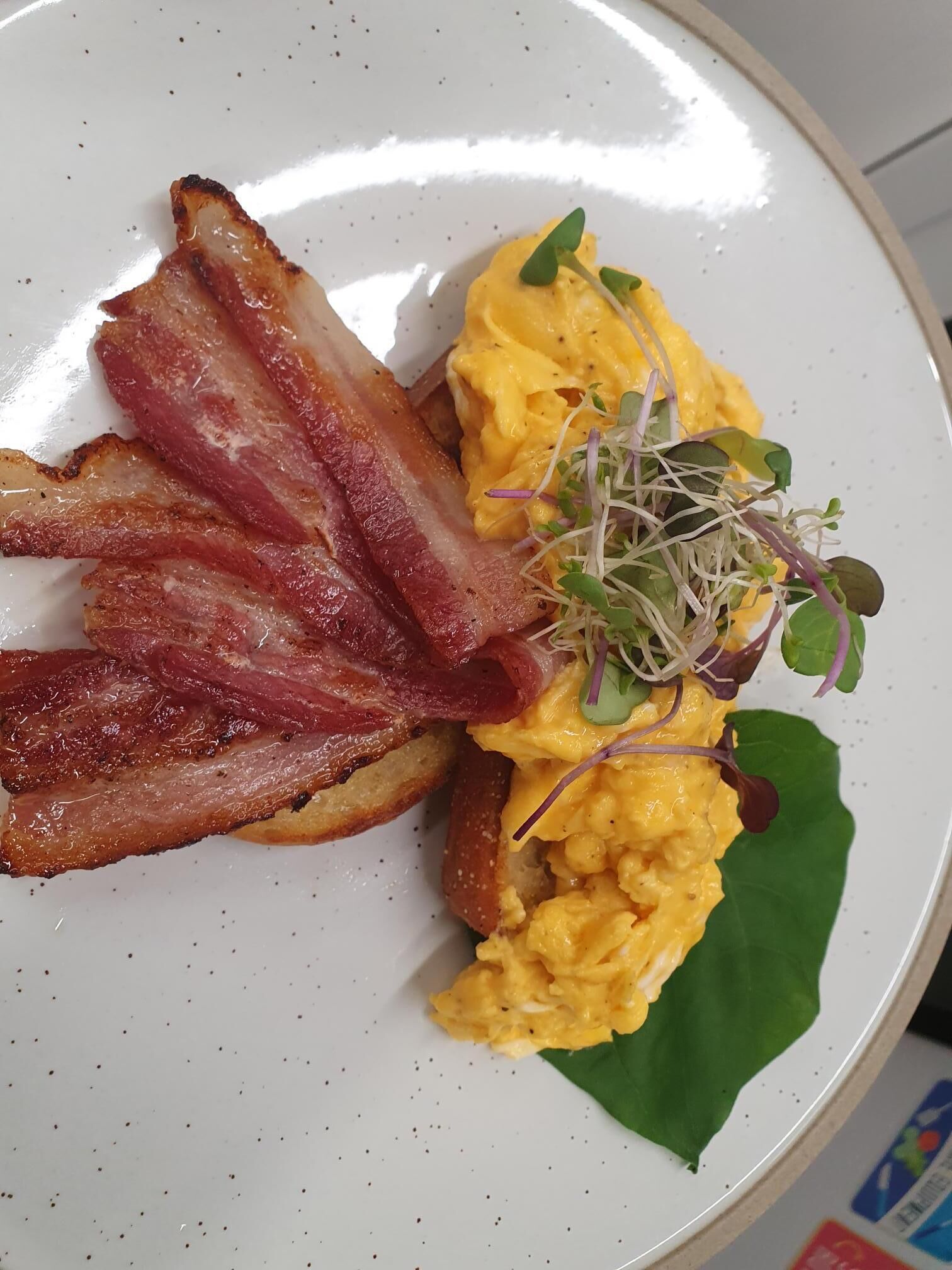 En tallerken med røræg, bacon og et grønt blad som pynt.