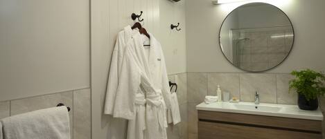 A bathroom with a white towel, a white robe hanging on a hook, a round mirror, a sink, and a potted plant.