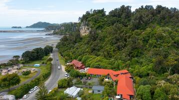 A coastal property with a road leading to a cluster of houses, a beach, and a forested hill.
