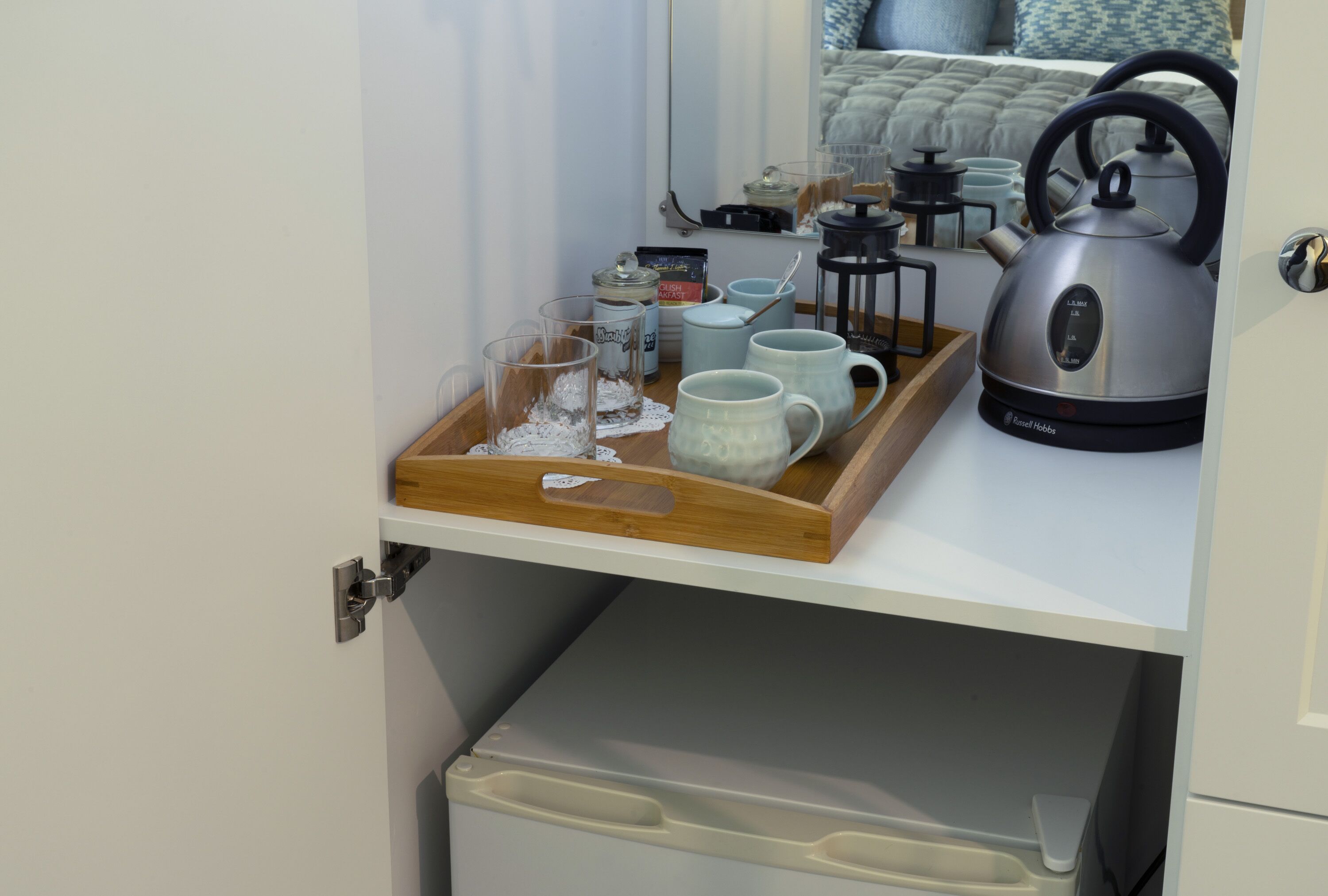 Een keukenhoek met een dienblad vol mokken, een waterkoker en een koffiezetapparaat op een aanrecht.