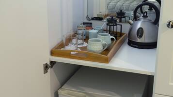 Een keukenhoek met een dienblad vol mokken, een waterkoker en een koffiezetapparaat op een aanrecht.