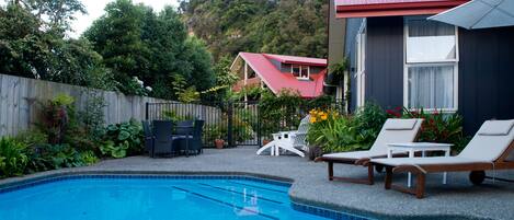 A backyard with a swimming pool, lounge chairs, and a wooden fence.