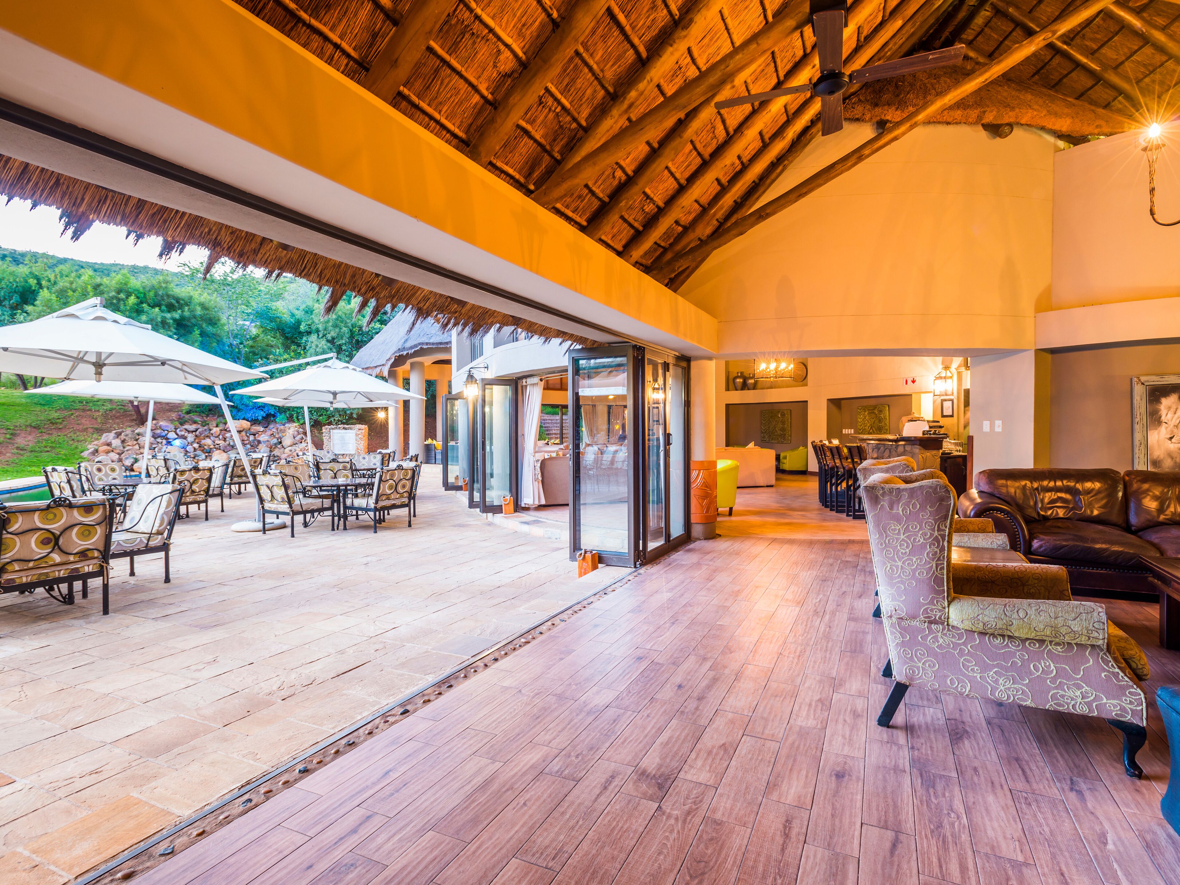 An open-plan living area with wooden flooring, outdoor seating, and a thatched roof.