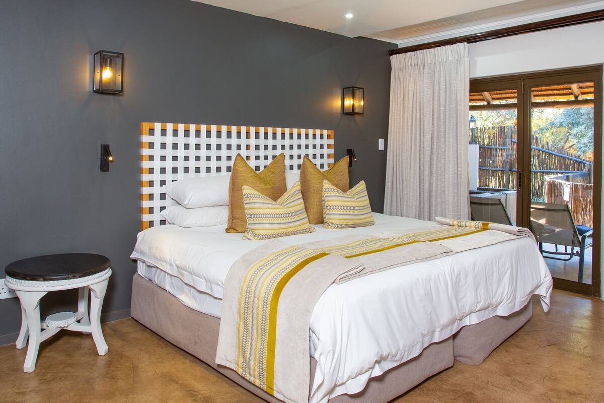 A bedroom with a bed, a small stool, and a view of an outdoor area.