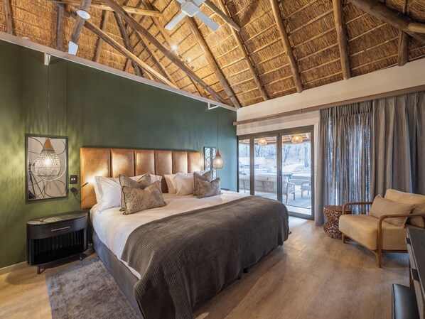 A bedroom with a large bed, a nightstand, a chair, and a view of the outdoors through a sliding door.