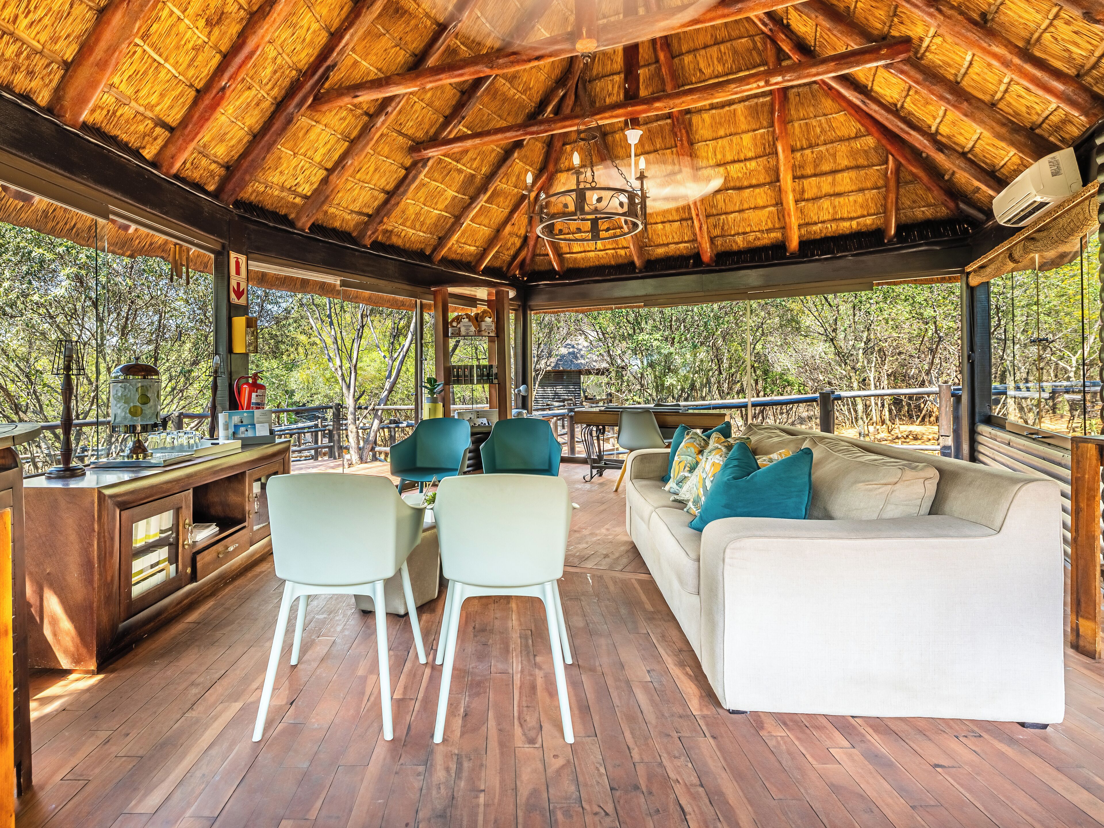 A wooden deck with a thatched roof, a sofa, chairs, and a dining area with a view of trees.