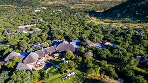 An aerial view of a resort with multiple thatched-roof cottages, a swimming pool, and lush greenery. - Ivory Tree Game Lodge (Pilanesberg National Park)