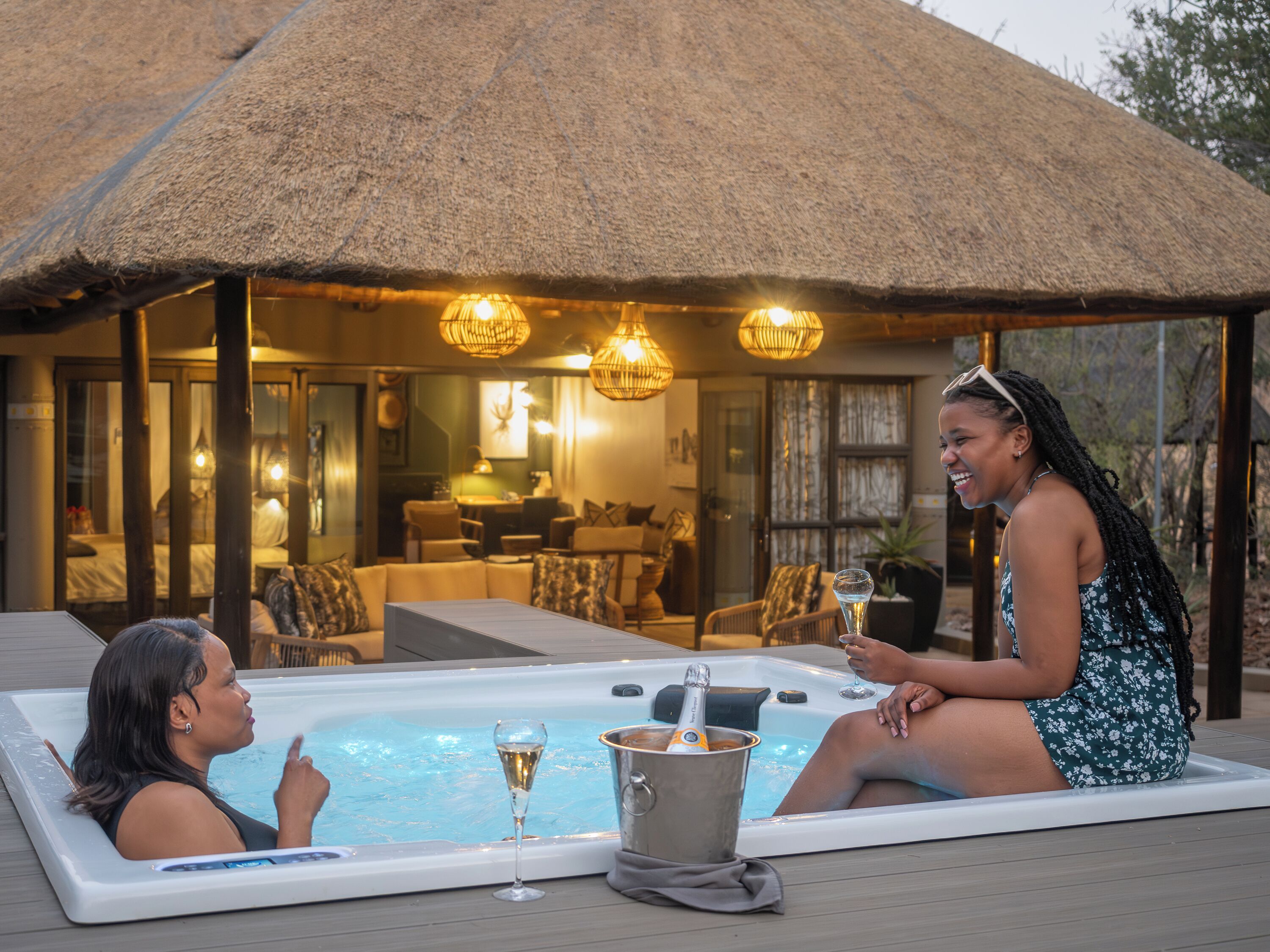 An outdoor hot tub with a thatched roof structure, a lounge area with seating, and a view of the surrounding landscape.