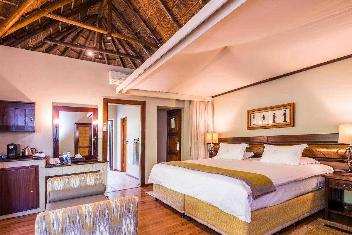 A hotel room with a bed, bedside table, lamp, and a desk with a chair.