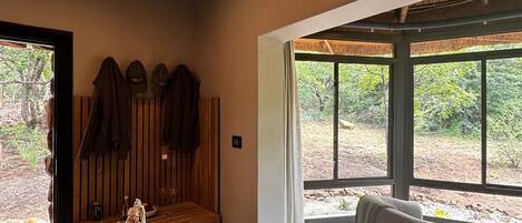 A room with a wooden bench, a hanging chair, and a table with a pot and utensils. There are windows with a view of greenery outside.