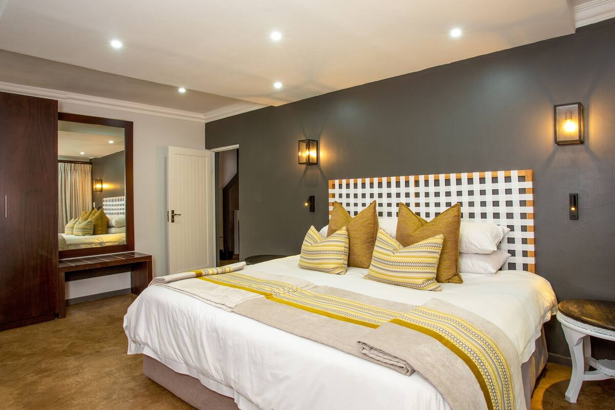 A bedroom with a large bed, a wooden headboard, a bedside table, and a mirror.