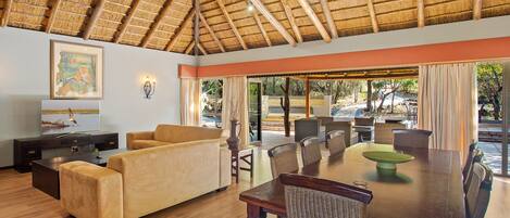 A spacious room with a high ceiling, a dining area with wicker chairs, a sofa, and a television on a cabinet.
