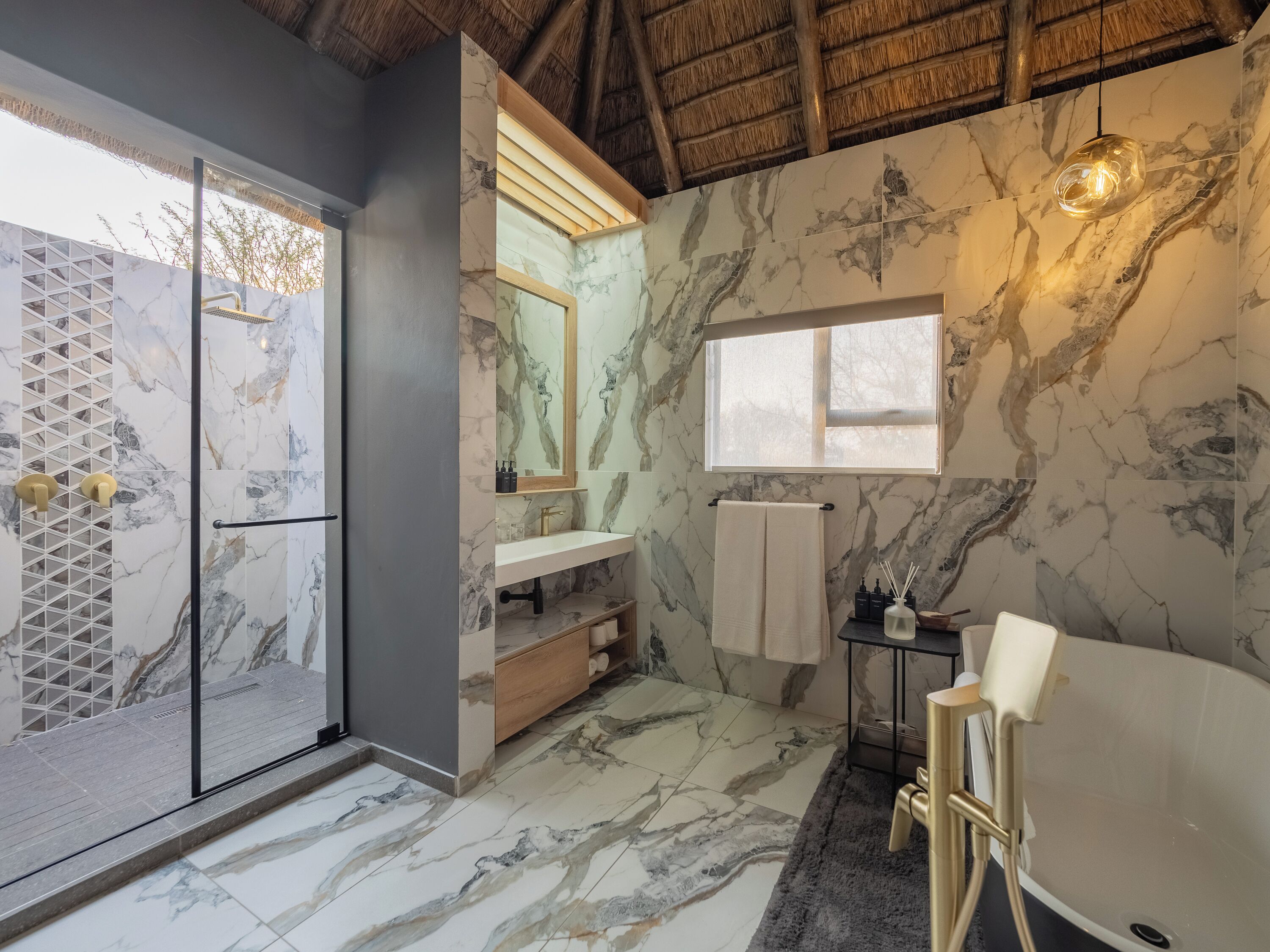 A bathroom with a marble floor, a glass shower enclosure, a vanity with a mirror, a bathtub, and a window.